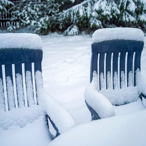 Zwei verschneite Gartenstühle aus Kunststoff im Wintergarten