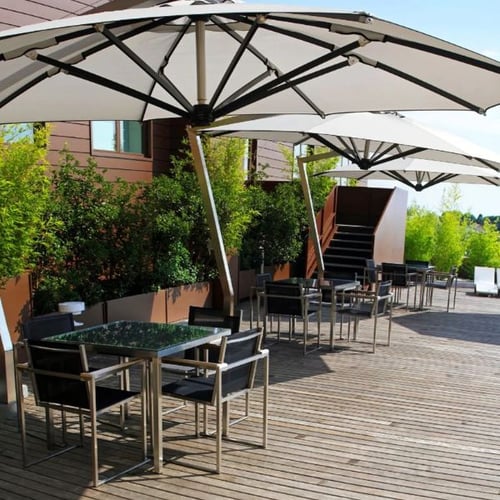 Große Dachterrasse mit Esstischen, schwarzen Stühlen und weißen Sonnenschirmen