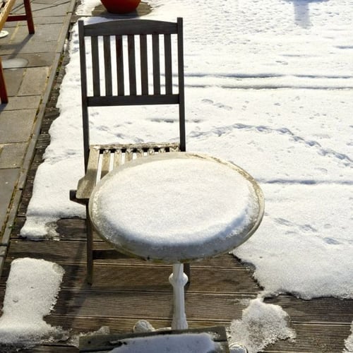 Gartenstuhl und runder Tisch mit Schnee auf Holzterrasse