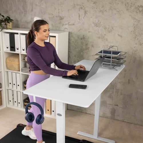 Frau arbeitet im Stehen am Laptop an einem weißen Schreibtisch mit integriertem Laufband