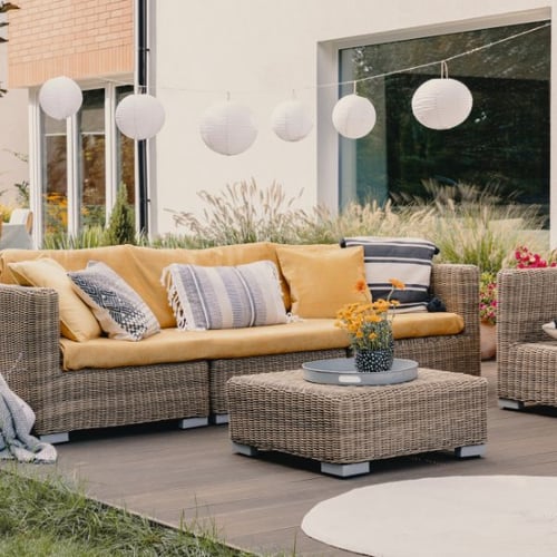 Geflochtene Gartensitzgruppe mit gelben Kissen und Hängelampen im Tageslicht