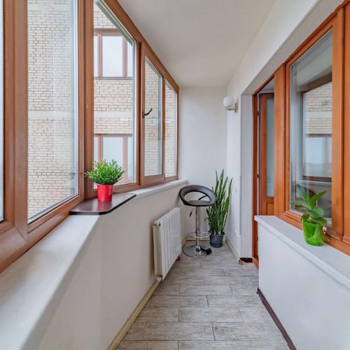 Schmale Loggia mit Pflanzen, Barhocker und großen Fenstern