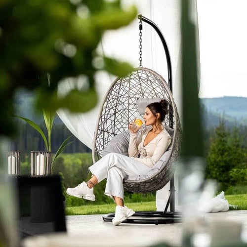 Frau im di volio Hängesessel auf moderner Terrasse mit Gartenblick