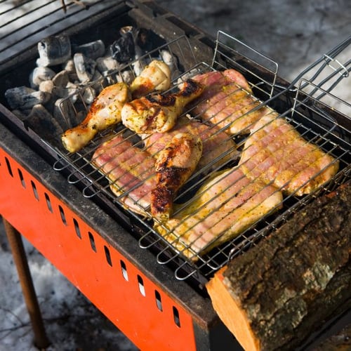 Gegrilltes Fleisch und Hähnchenschenkel auf einem Holzkohlegrill mit rotem Korpus im Freien, im Winter.