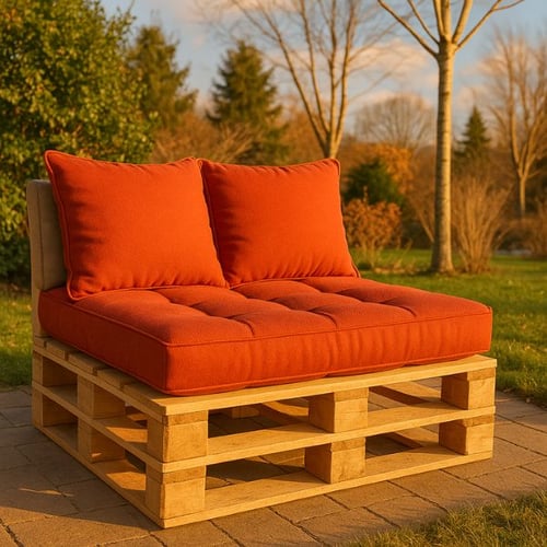 Sitzbank aus Paletten mit orangen Kissen auf Steinplatten im Garten bei Sonnenuntergang