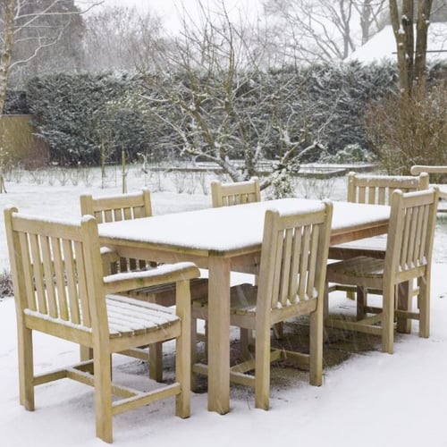 Garten-Essgruppe aus Holz im Winter, bedeckt mit Schnee. Der Tisch und die Stühle stehen auf einer verschneiten Terrasse im Garten.