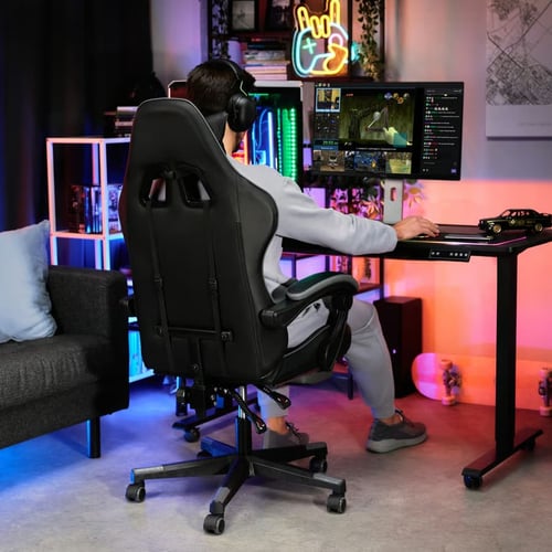 Gracz siedzący na ergonomicznym czarnym fotelu gamingowym w trakcie rozgrywki przy biurku LED – propozycja dla tych, którzy szukają odpowiedzi na pytanie: jaki fotel gamingowy do 500 zł zapewni komfort w trakcie grania.