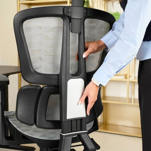 Zbliżenie na regulację ergonomicznego fotela biurowego z siatkowym oparciem – kobieta dostosowuje wysokość podparcia lędźwiowego. Idealny przykład, jaki fotel ergonomiczny do komputera wybrać dla zdrowia kręgosłupa.