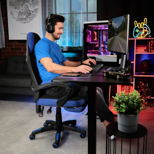 Gracz w niebieskiej koszulce siedzi przy biurku na ergonomicznym fotelu gamingowym z wysokim oparciem i słuchawkami na uszach, grając na komputerze – inspiracja dla tych, którzy szukają odpowiedzi na pytanie, jaki fotel gamingowy wybrać do intensywnego grania.